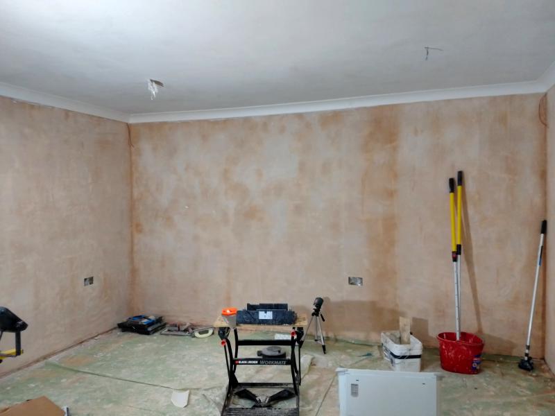 View of the right wall and ceiling. Coving is installed where the wall meets the ceiling. It is a concave shape about 10 centimetres to a side. In the corners of the room, black and red wires protrude slightly offset from the very corner, underneath the coving.