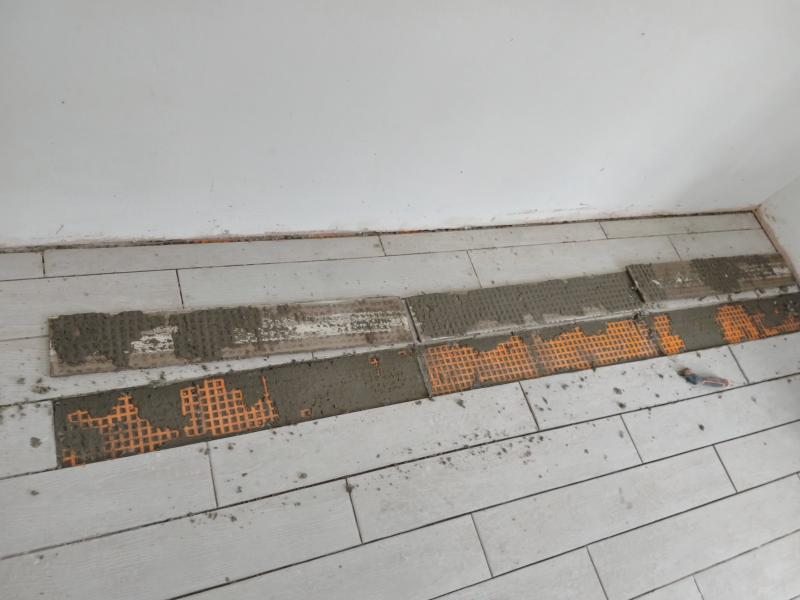 Three tiles lay upside down on an otherwise fully tiled floor, showing patchy mortar. Where they came from, the orange subfloor and more patchy mortar is shown.