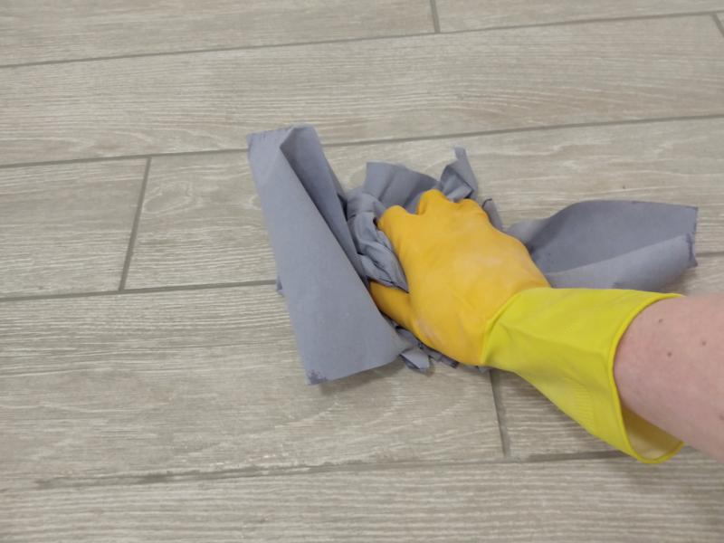 A yellow later-gloved hand wipes water off tiles with bunched up blue paper towels