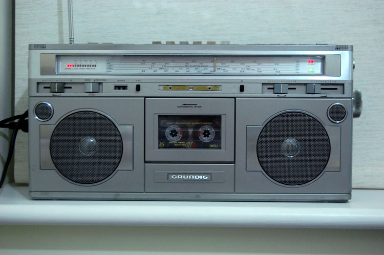 Frontal photo of the radio before any alterations were made, showing buttons on top, speakers on either side of a cassette deck, slider buttons, a radio tuning dial across the top, and sound volume indicator lights