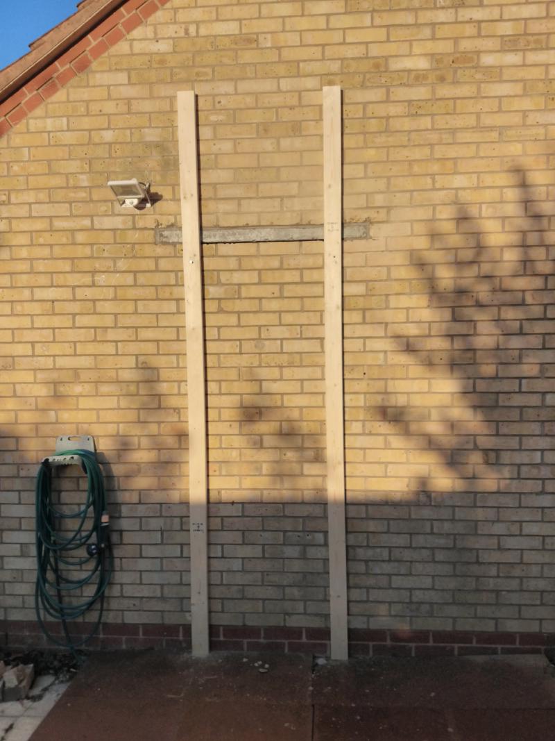 Outside view of the wall. Overlapping the lintel on the left and right, 3 metre long wooden beams are vertically mounted to the wall.