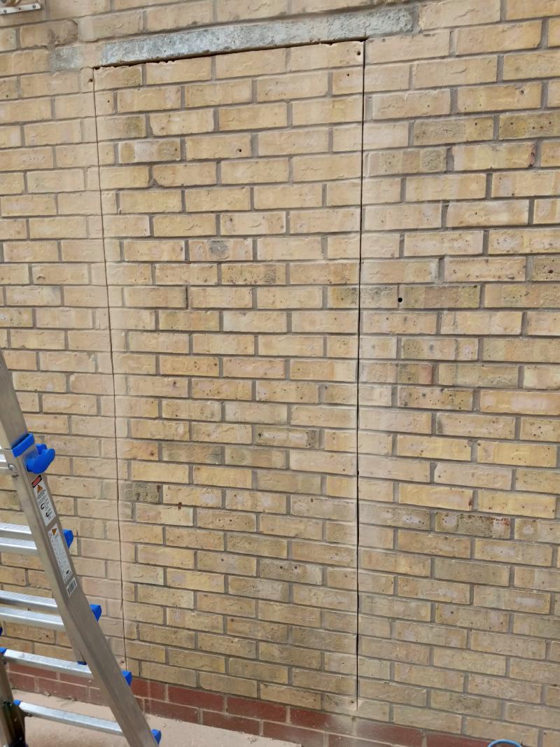 View of the wall, with vertical cuts made from right under the lintel down to differently-coloured bricks by the bottom