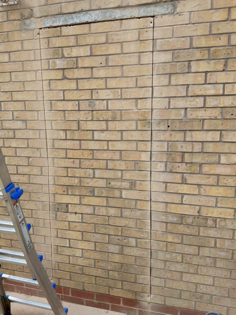 View of the wall, with vertical cuts made from right under the lintel down to differently-coloured bricks by the bottom