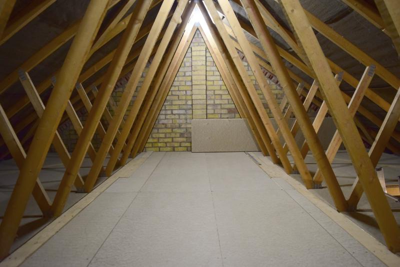 View of the centre of the finished loft space. The trusses form an upside down V in the middle, and where those trusses meet the floor, another one starts towards the slope of the roof. The floor is, you guessed it, fully made of fibre board.
