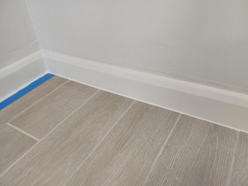 Closeup of a corner of skirting board where the largest section has the masking tape removed, showing a clean straight edge to the sealant