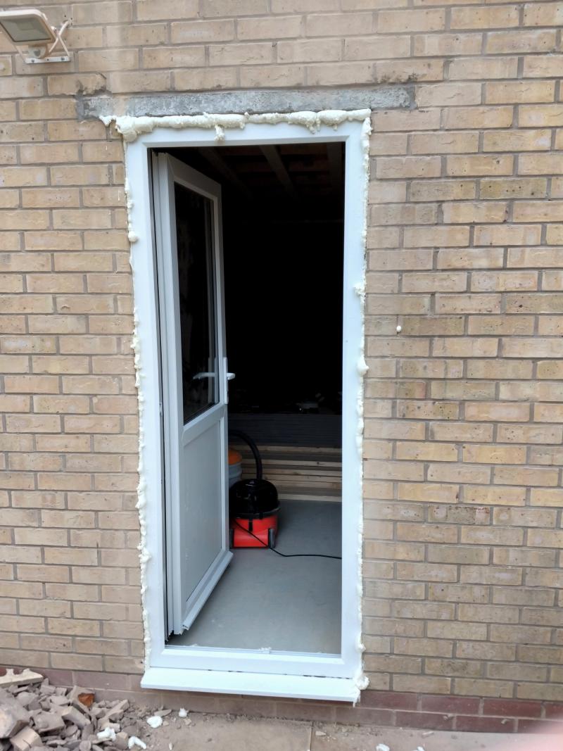 Newly installed side door, this time opened. Between the frame of the door and the brickwork/lintel, there's a pale expanding foam protruding.