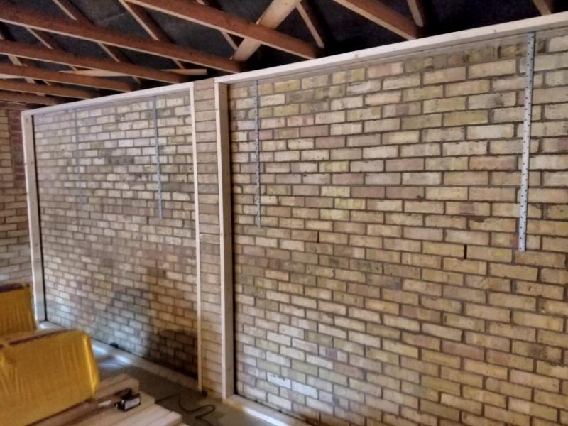 Rear wall of the garage, including a column of extra bricks in the middle. Two square of wooden beams are constructed, one to either side of that brick column.
