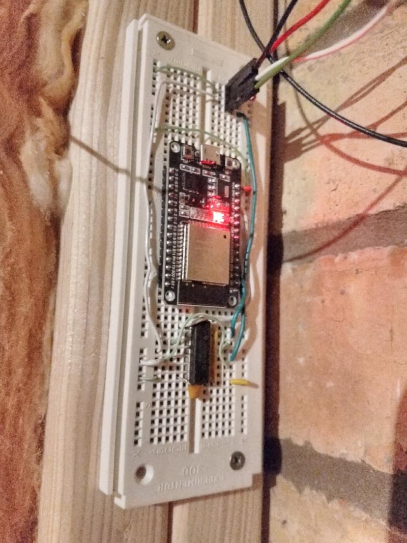 A breadboard (white plastic slab with loads of small holes in a grid pattern to allow connecting electronic components without soldering) is screwed into wooden beams. On the breadboard is a black board carrying som circuitry and a large metal-cased component (the ESP32 dev board). Underneath is a single chip, a small capacitor and a bunch of wires. At the top are 4 wires plugged into the breadboard, leading away from the board and to the LEDs (out of frame)