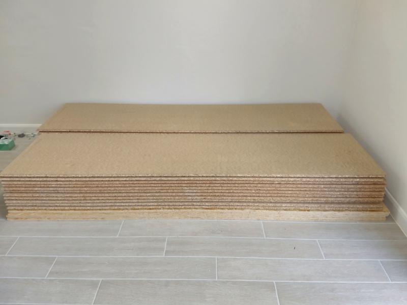 A stack of engineered floorboard in the corner of the garage. On the bottom of the stack are a smaller number of thin chipboard sheets.