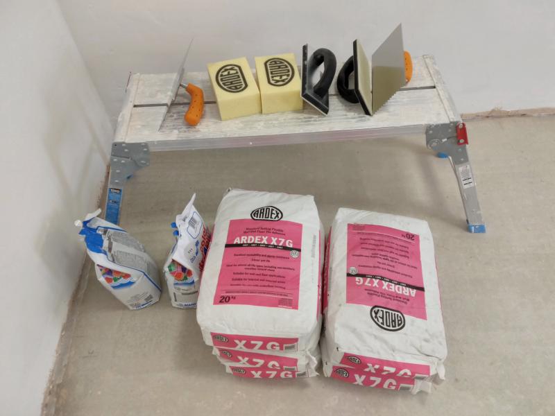 Work platform with tiling trowels, 'Ardex' tile cleaning sponges, floats; on the floor: two bags of grout, 5 bags of 'Ardex X7G' Mortar