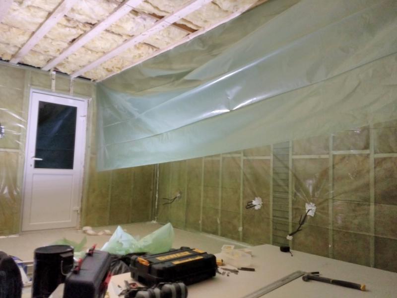 Wide view of a corner of the garage. The walls are covered in translucent green plastic sheeting. Where cables protrude, there's a path of reflective tape surrounding the cable. Where the sheeting meets the floor, there is also reflective tape. On the ceiling, a partially hung sheet is seen, with half of it dangling down.