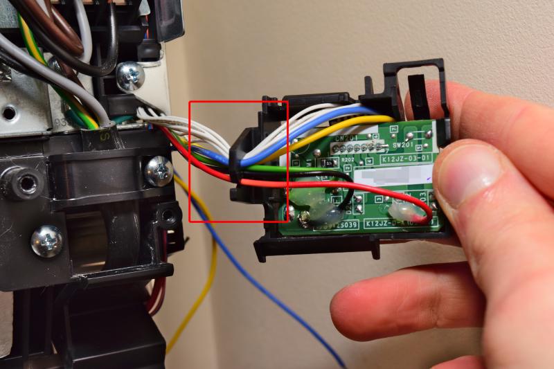 Reverse side of the module showing the modified PCB. At the top where the existing wires going to the connector reach behind the board, there are a yellow and a blue wire as well, leading to the LED. The wires soldered to the board as well as the LED wires are organized into the plastic hook on the left.