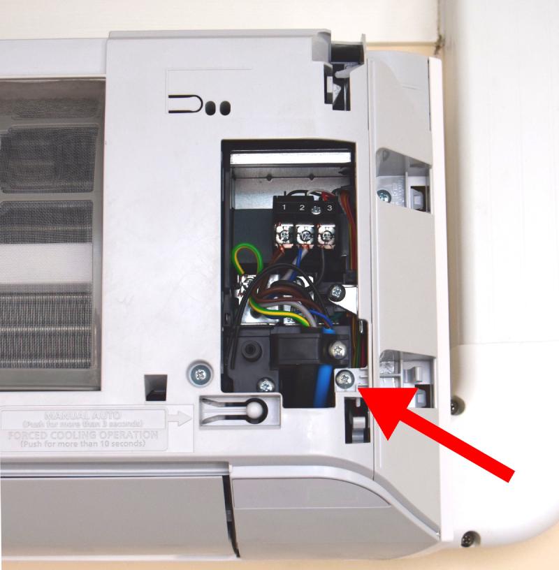 Closeup of the AC unit where the terminals cover is removed. In the bottom right there's a now-revealed screw.