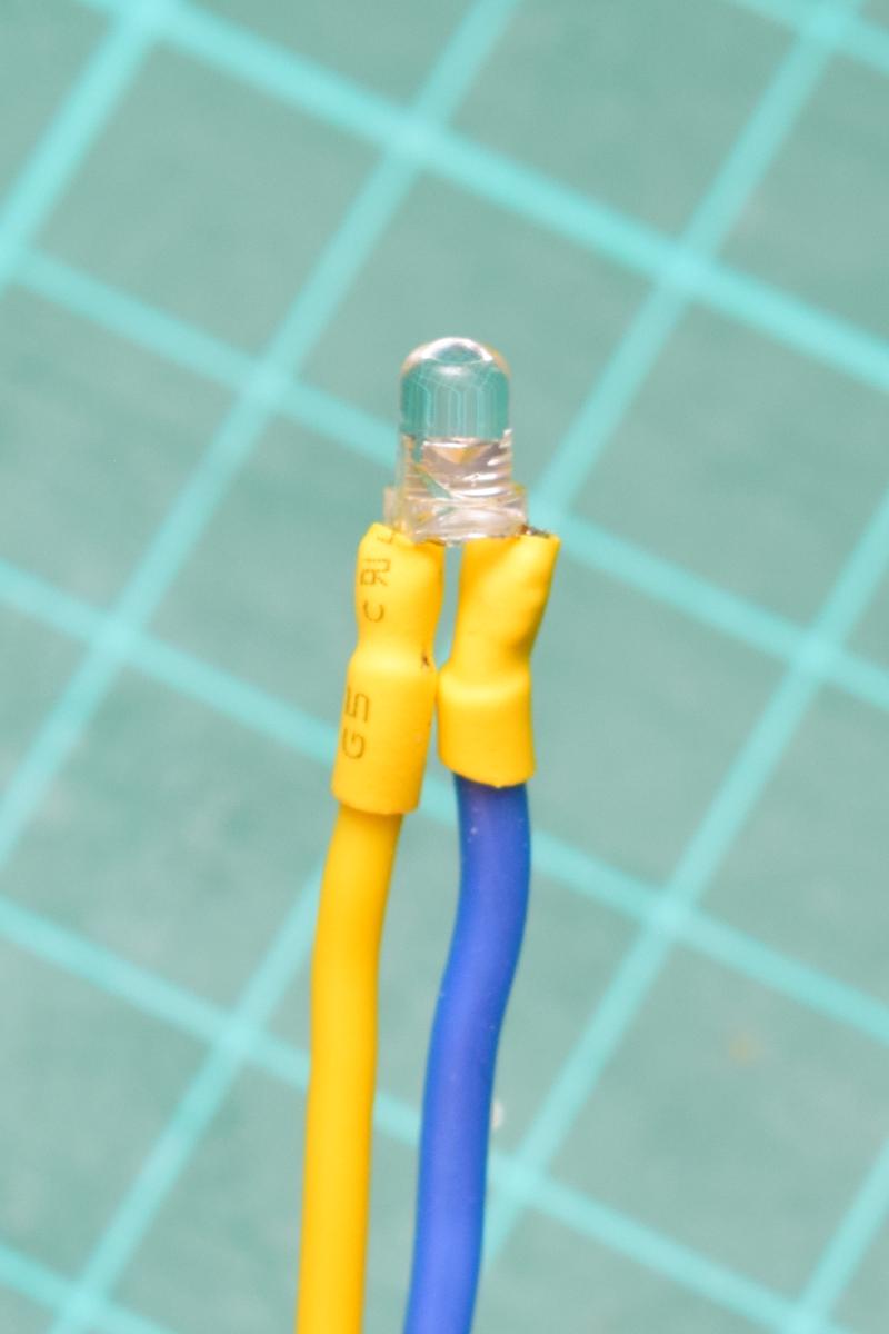 Close-up of a 3 millimetre infared LED wired with yellow and blue wires. The heat-shrink insulation reaches right up to the edge of the LED itself.