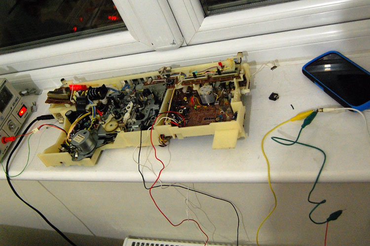 Photo of the innards of the radio wired up to a bench power supply. A black, red and white wire hang down from the radio and are connected to an audio cable coming from a phone by crocodile clips
