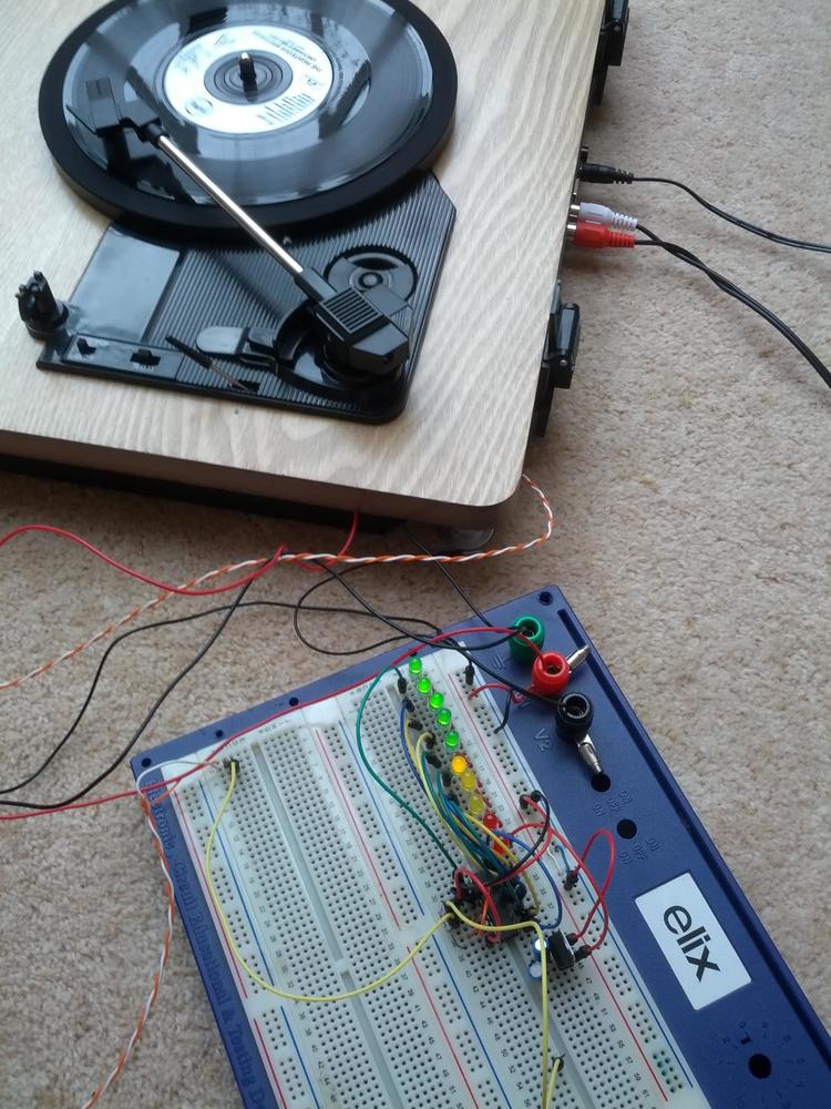 Turntable playing a record, with wires coming out of it, connected to breadboard with messy circuit, some LEDs lit up